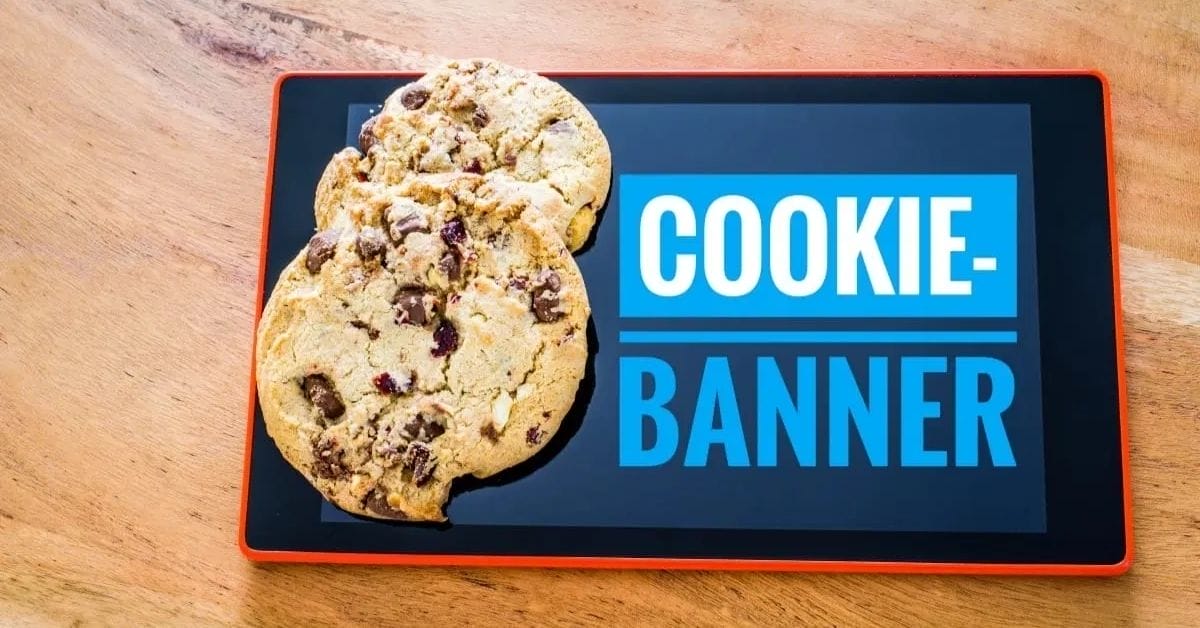 Two chocolate chip cookies partially cover a tablet screen displaying the words "COOKIE-BANNER" in bold blue and white text—a playful nod to the cookie policy for website notifications.