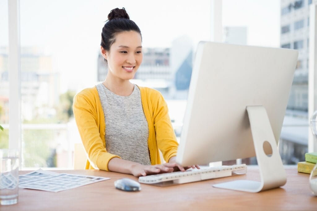 A young Asian woman providing services at a desk in front of a computer.