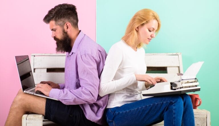 A couple working on laptops on a park bench.