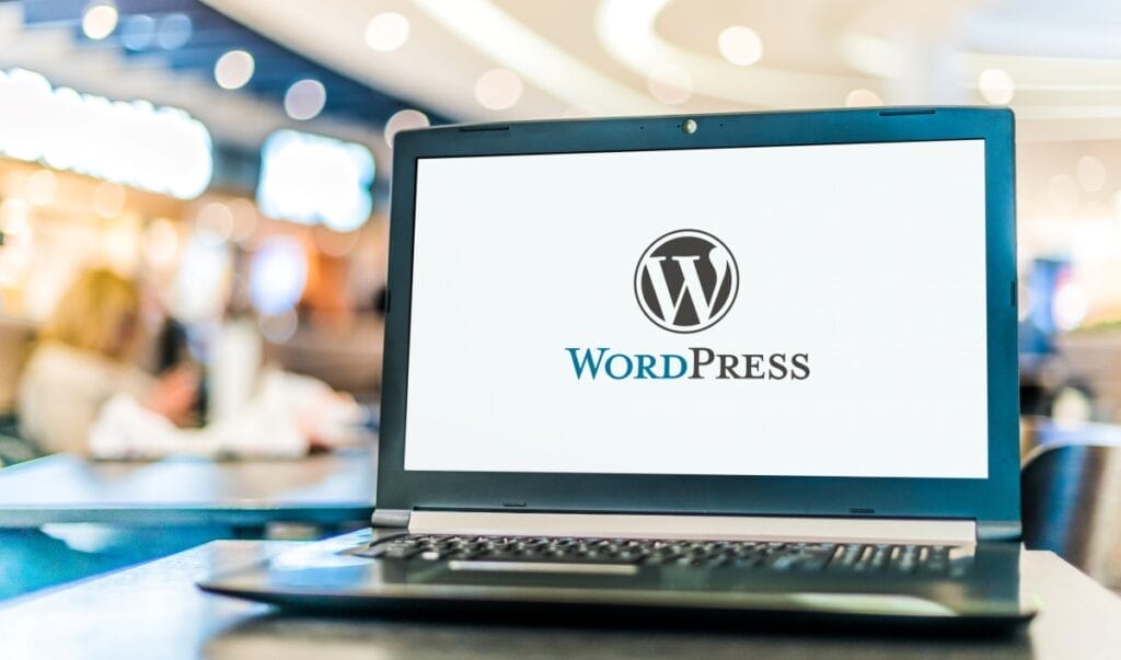 Laptop displaying WordPress logo, a popular website builder, in a busy cafe setting.