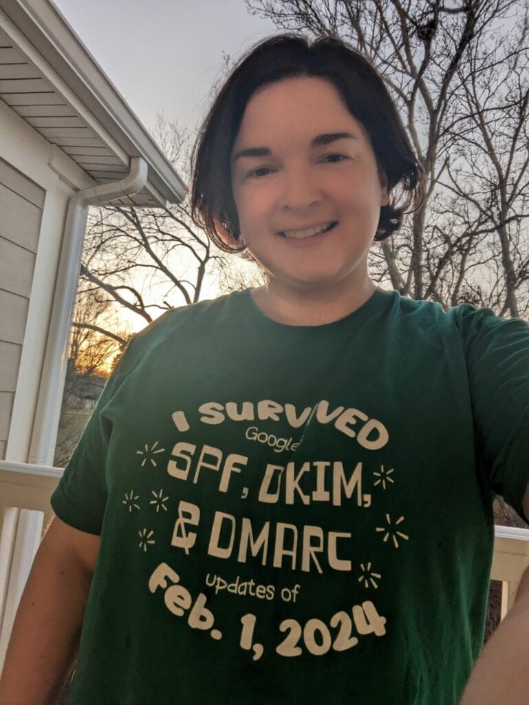 A person smiling outdoors, wearing a green t-shirt with text that reads "I survived Google's SPF, DKIM, & DMARC updates of Feb. 1, 2024 - thanks to