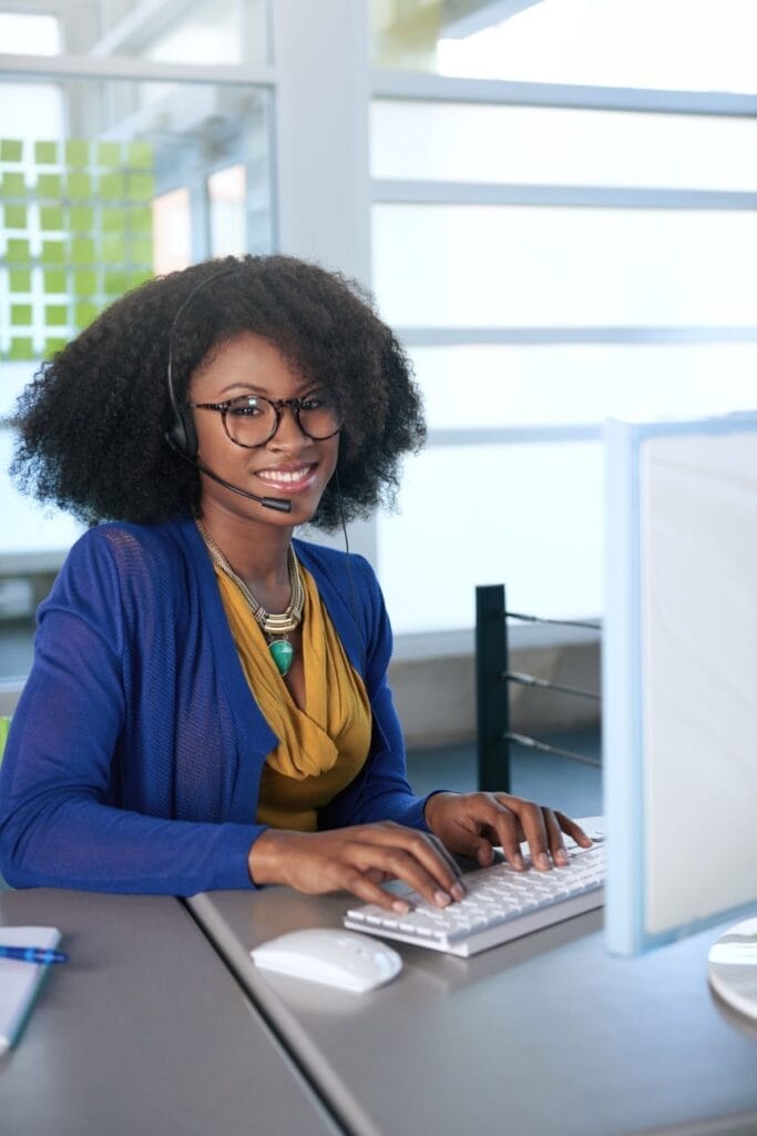 Person wearing glasses and a headset, seated at a desk in a modern office space, typing with a smile as they manage Care Plans on WordPress.