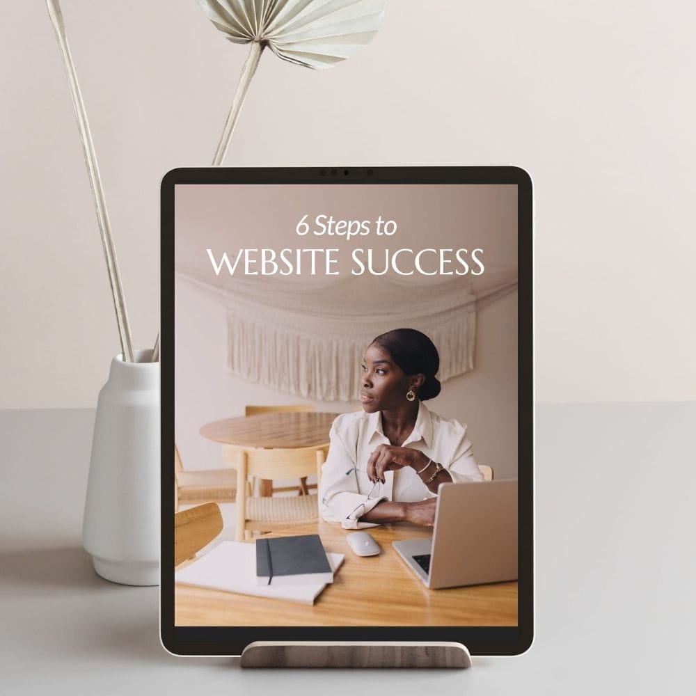 Tablet on a stand displaying a guide titled "6 Steps to Website Success" with an image of a seated person in a home office setting.