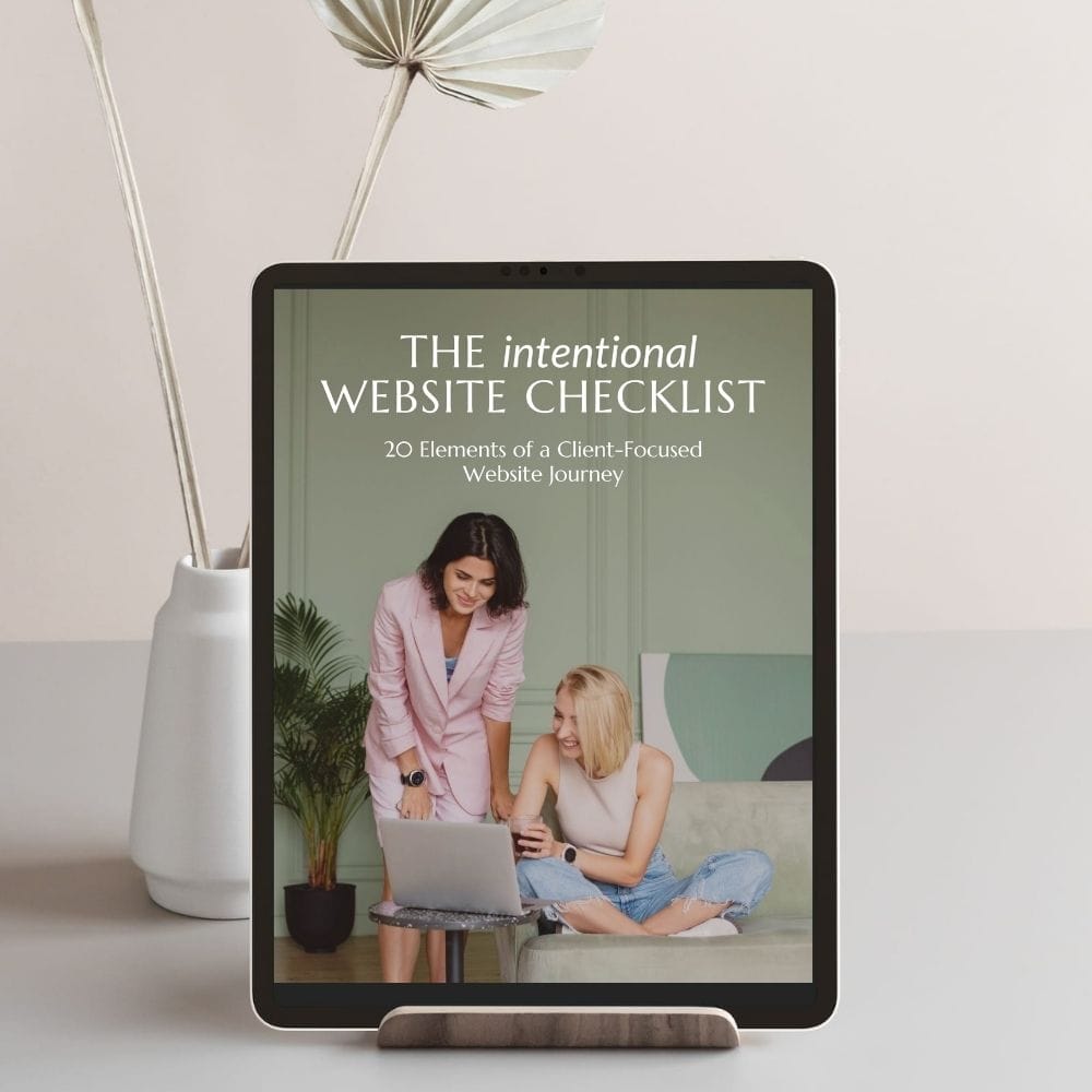 Tablet displaying "The Intentional Website Checklist" cover, featuring two women looking at a laptop. In the background, a vase with decorative items is visible.