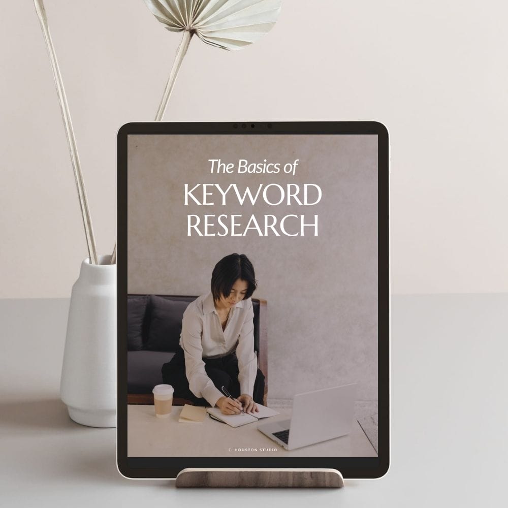 E-book titled "The Basics of Keyword Research" displayed on a tablet, with a picture of a person writing at a desk beside a laptop.