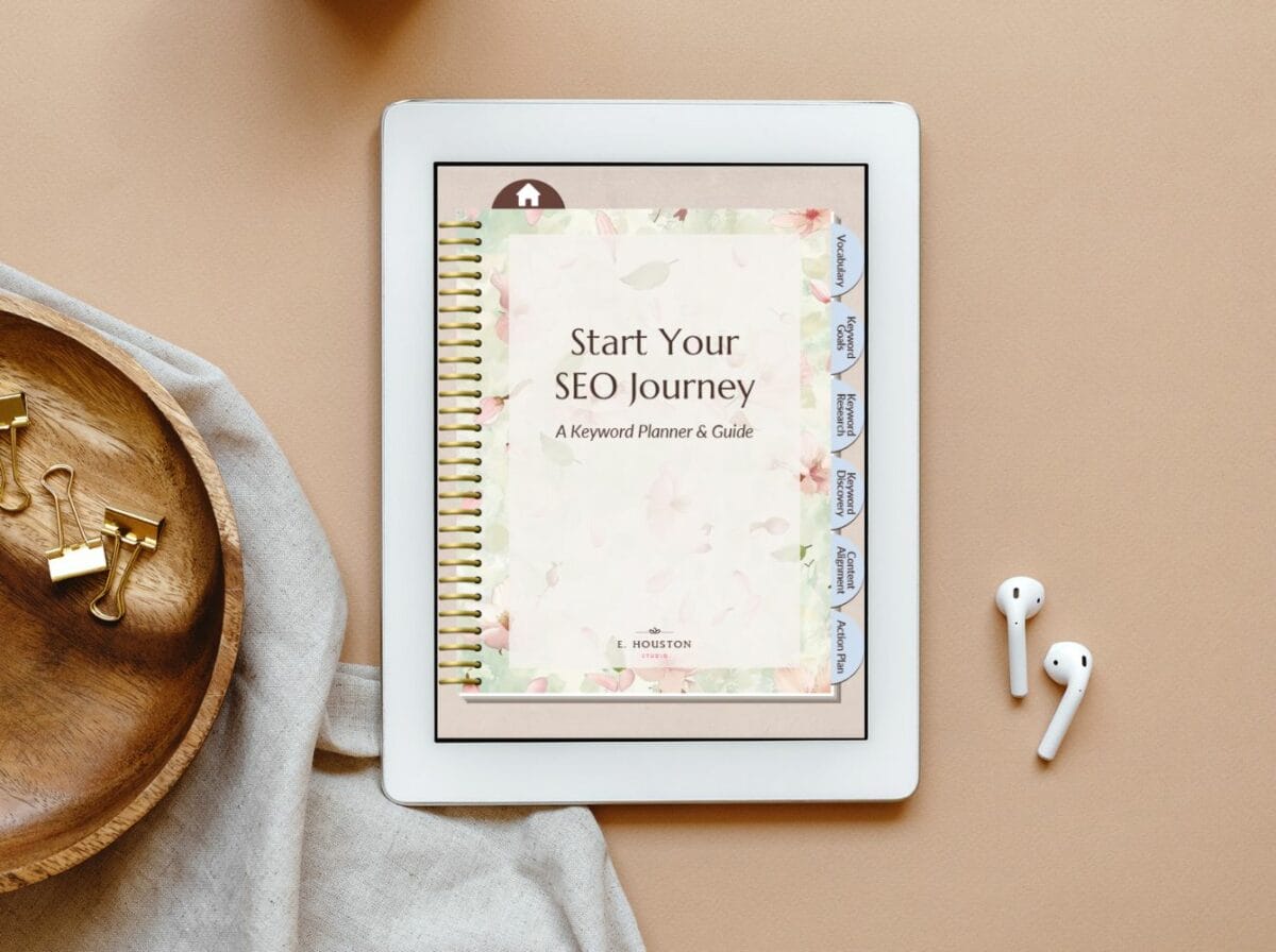An iPad displays a digital notebook titled "Start Your SEO Journey: A Keyword Planner & Guide." The tablet is on a beige surface beside AirPods, a wooden tray, and office supplies.