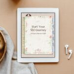 An iPad displays a digital notebook titled "Start Your SEO Journey: A Keyword Planner & Guide." The tablet is on a beige surface beside AirPods, a wooden tray, and office supplies.