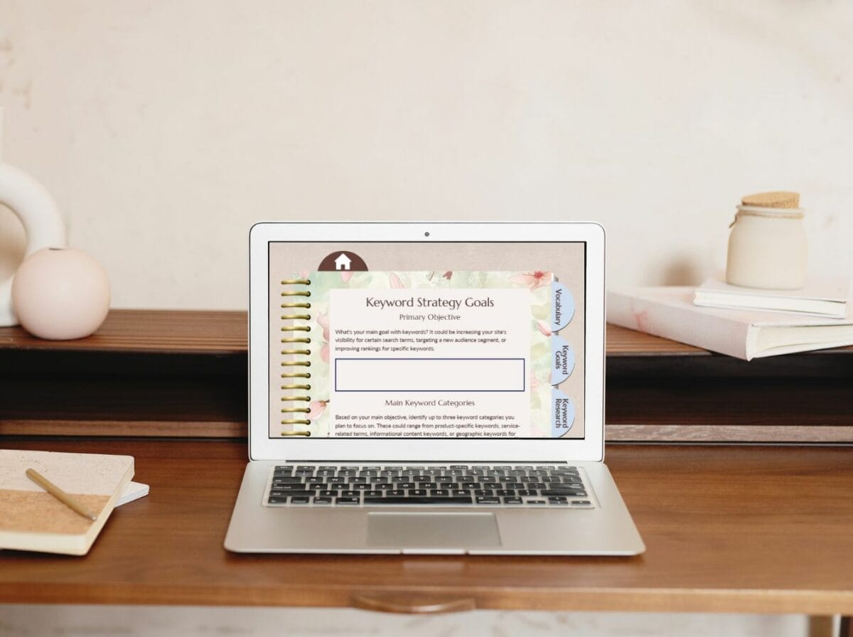 A laptop on a wooden desk displays a webpage titled "Keyword Strategy Goals." Nearby are a notebook, pen, and decorative items.