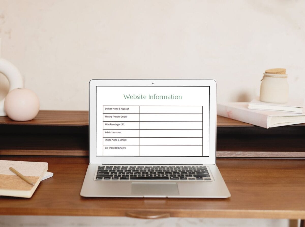 A laptop on a wooden desk displays a website information table with categories such as domain name, hosting details, and installed plugins.