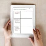 Person holding a tablet displaying a quarterly maintenance checklist with sections for updates, compliance check, and requirements. The form has blank spaces for notes and a date field.