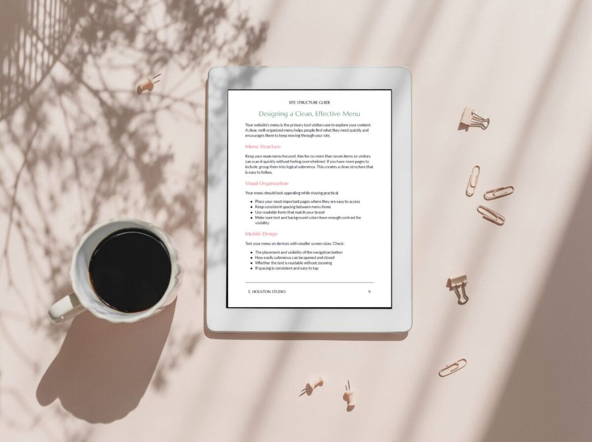 A tablet displaying a guide on menu structure rests on a beige surface beside a cup of black coffee, paper clips, and scattered push pins, with leaf shadows cast across the scene.